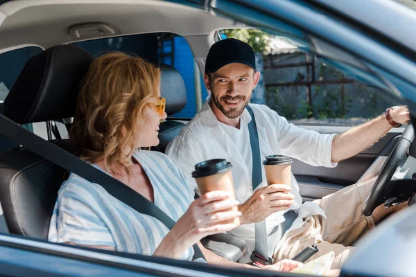 Enfoque selectivo de hombre y mujer alegre sosteniendo vasos de papel en el coche - foto de stock