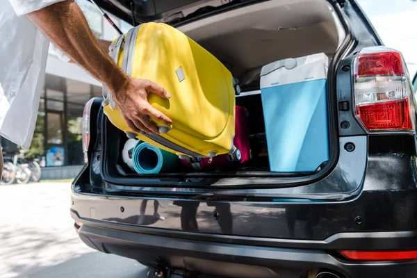 Visão cortada do homem colocando bagagem amarela no porta-malas do carro — Fotografia de Stock