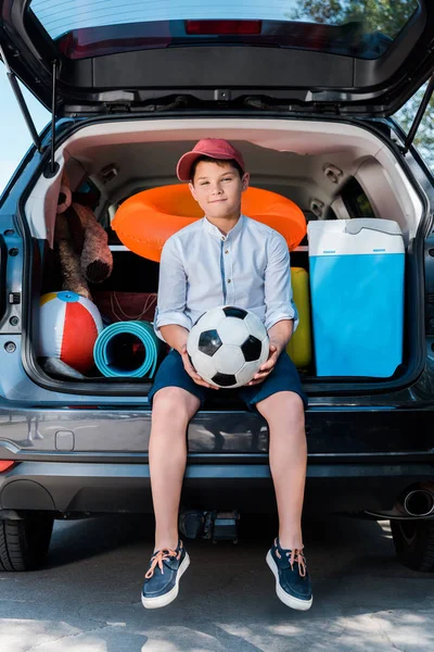 Happy child holding football while sitting and looking at camera — Stock Photo