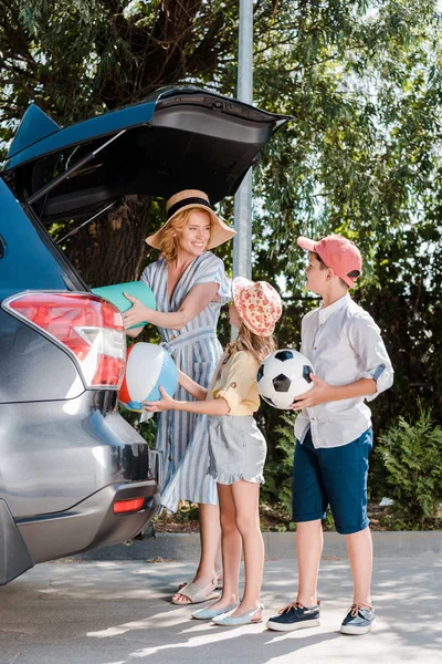 Весела мати в солом'яному капелюсі дивиться на дітей біля машини — стокове фото