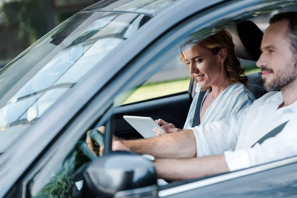 Selective focus of man driving car while woman holding digital tablet — Stock Photo