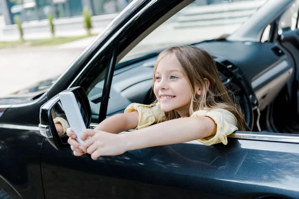 Foyer sélectif de l'enfant heureux prenant selfie sur smartphone tout en étant assis dans la voiture — Photo de stock