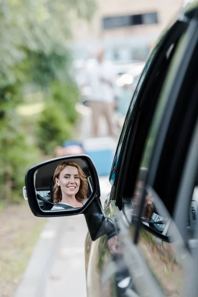 Избирательный фокус веселой женщины, смотрящей на окно автомобиля и улыбающейся в автоматическом режиме — стоковое фото