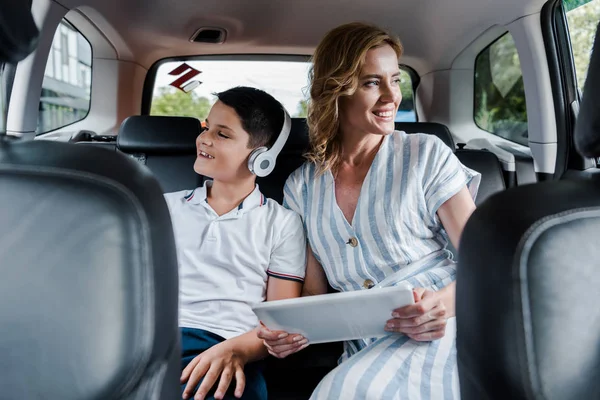 Foyer sélectif de l'enfant heureux dans les écouteurs près de la mère avec tablette numérique dans la voiture — Photo de stock