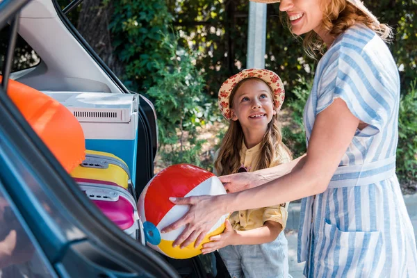 Ausgeschnittene Ansicht einer glücklichen Frau, die Strandball in Auto in der Nähe ihrer Tochter platziert — Stockfoto