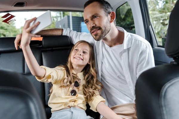 Selective focus of happy kid talking selfie with father in car — Stock Photo