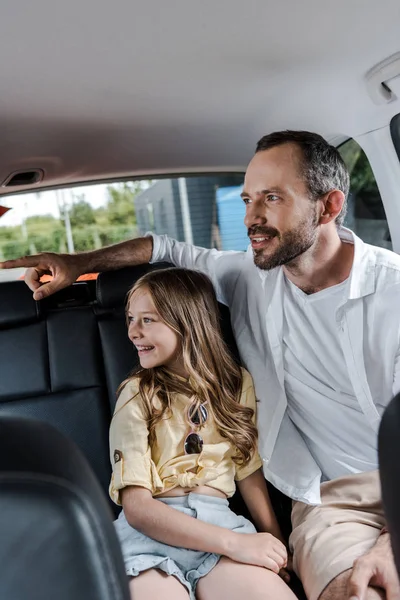 Selective focus of bearded pointing with finger near daughter in car — Stock Photo