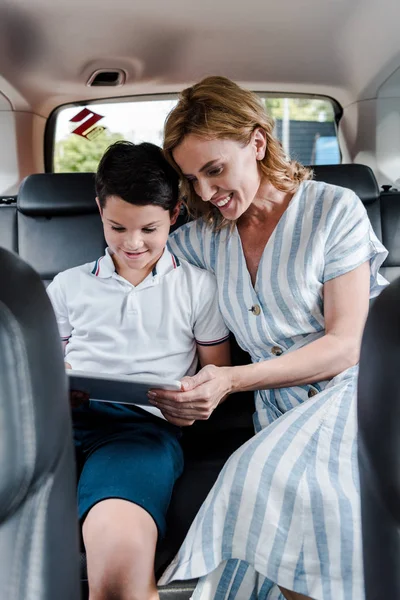Selective focus of happy mother and son using digital tablet in car — Stock Photo