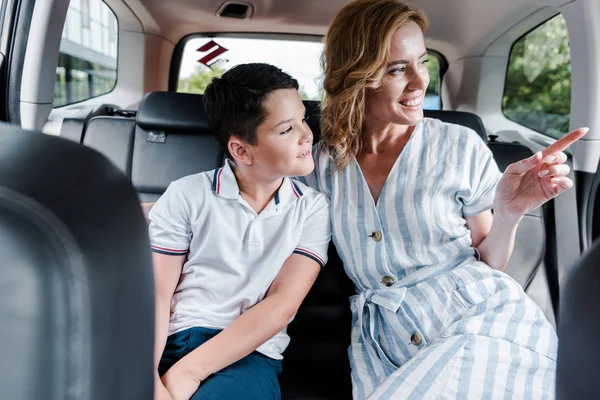 Selective focus of cheerful mother pointing with finger near son in car — Stock Photo
