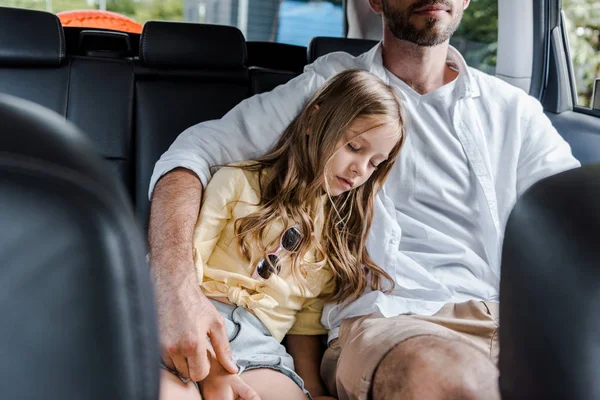 Vue recadrée du père assis dans la voiture près de fille mignonne avec les yeux fermés — Photo de stock