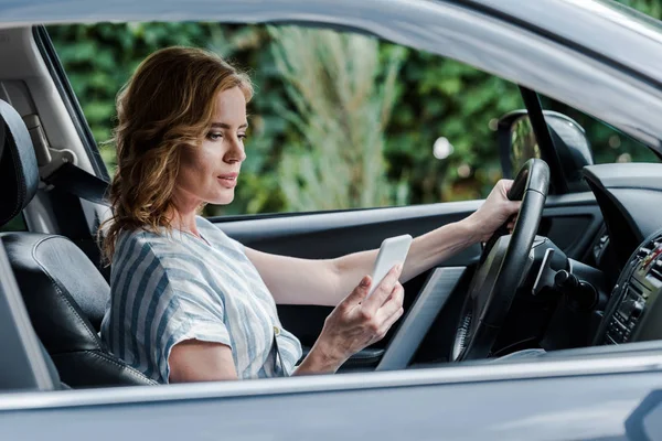 Enfoque selectivo de la mujer atractiva usando el teléfono inteligente mientras conduce el coche - foto de stock