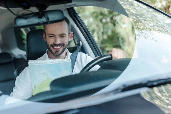 Selektiver Fokus des glücklichen Mannes, der Auto fährt und auf die Karte schaut — Stockfoto