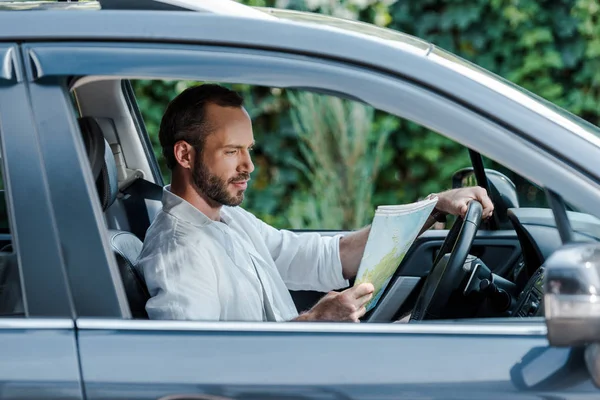 Selective focus of bearded man driving car and looking at map — Stock Photo