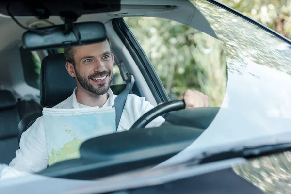 Selektiver Fokus des bärtigen und glücklichen Mannes, der Auto fährt und auf die Landkarte schaut — Stockfoto