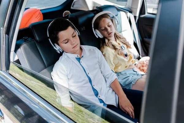 Foco seletivo de crianças bonitos em fones de ouvido dormindo no carro — Fotografia de Stock