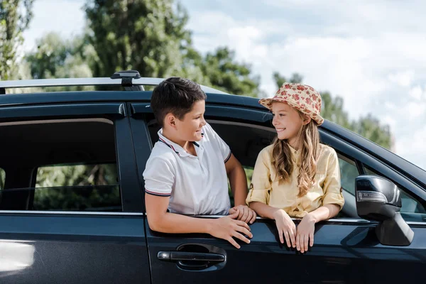 Niño feliz en sombrero de paja mirando hermano desde la ventana del coche - foto de stock