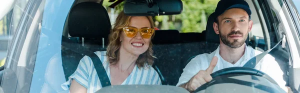 Tiro panorâmico de mulher feliz perto do homem no carro de condução cap — Fotografia de Stock