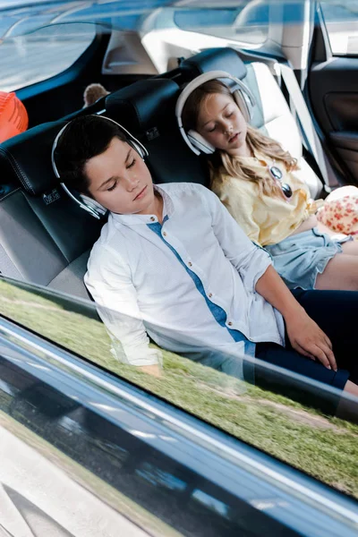 Selective focus of cute children in headphones sleeping in car — Stock Photo