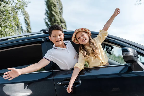 Vista de ángulo bajo de niños felices con las manos extendidas en las ventanas del coche - foto de stock