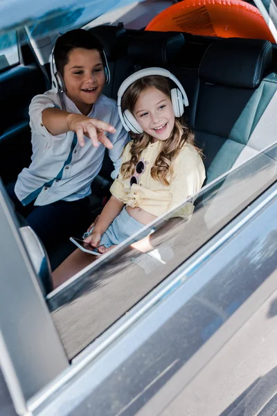 Selektiver Fokus des glücklichen Kindes, das mit dem Finger auf Schwester im Kopfhörer zeigt — Stockfoto
