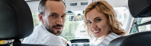 Панорамный снимок счастливого мужчины и женщины, улыбающихся сидя в машине — стоковое фото