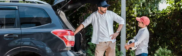 Panoramic shot of father standing with hand on hip near son with football — Stock Photo