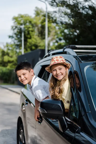 Soeur heureuse et frère regardant la caméra des fenêtres de la voiture — Photo de stock