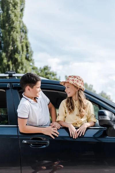 Счастливый брат смотрит на сестру в соломенной шляпе в машине — стоковое фото