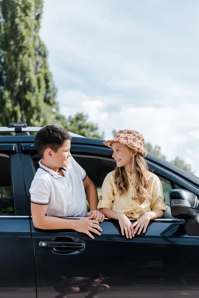 Feliz hermano mirando hermana en paja sombrero en coche - foto de stock