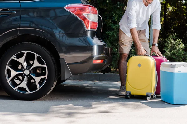 Vue recadrée de l'homme barbu debout près des bagages jaunes près de la voiture — Photo de stock
