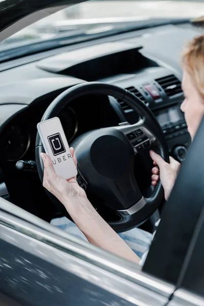 KYIV, UKRAINE - 26 JUIN 2019 : vue recadrée d'une femme tenant un smartphone avec une application uber à l'écran dans une voiture — Photo de stock