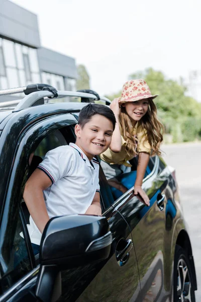 Enfoque selectivo de feliz hermano y hermana mirando a la cámara desde las ventanas del coche - foto de stock