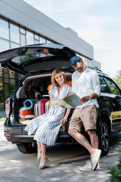 Bel homme en chapeau debout et tenant la carte près de la femme et de la voiture — Photo de stock