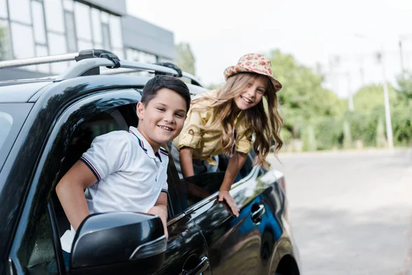 Selective focus of positive brother and sister looking at camera from car windows — Stock Photo