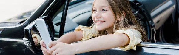 Panoramaaufnahme von fröhlichem Kind, das Selfie aus dem Autofenster macht — Stockfoto
