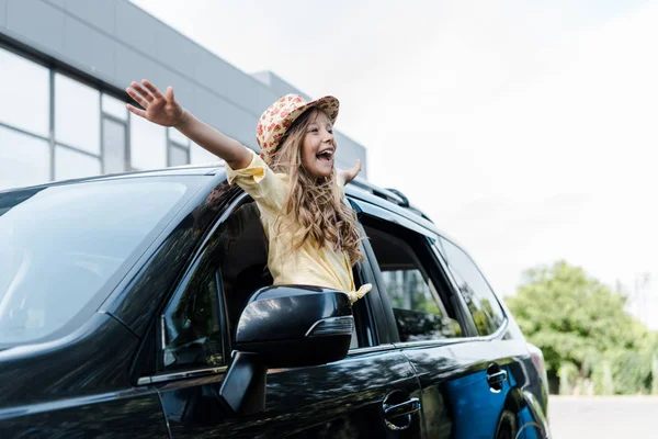 Glückliches Kind mit Strohhut und ausgestreckten Händen im Autofenster — Stockfoto