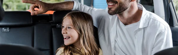 Panoramic shot of bearded pointing with finger near daughter in car — Stock Photo