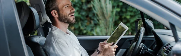 Панорамний знімок щасливого чоловіка, що тримає цифровий планшет у машині — стокове фото