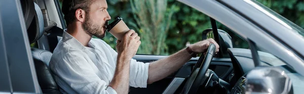 Panoramic shot of man drinking coffee to go while driving car — Stock Photo