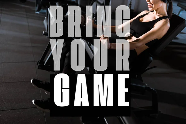 Cropped view of athletic woman exercising on training apparatus in gym with bring your game illustration — Stock Photo