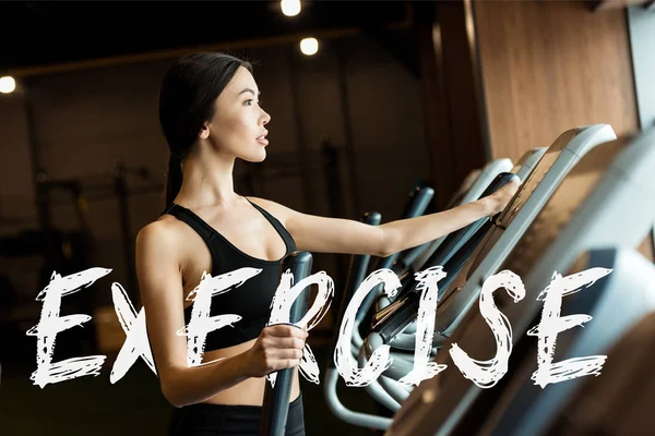 Selective focus of attractive woman in sportswear working out on exercising bike  with exercise illustration — Stock Photo