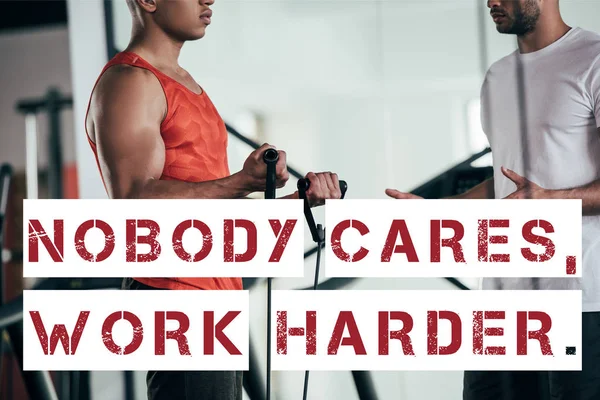 Partial view of trainer and african american sportsman near illustration with nobody cares, work harder inscription — Stock Photo