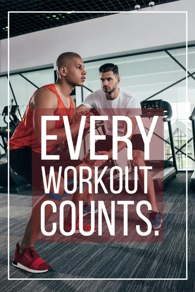 Attentive trainer supporting african american sportsman near illustration with every workout counts inscription — Stock Photo