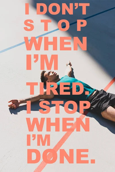 Mixed race sportsman laying on running track and spread arms with i dont stop when i am tired, i stop when i am done lettering — Stock Photo