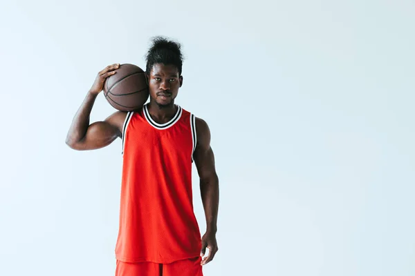Selbstbewusster afrikanisch-amerikanischer Basketballspieler blickt in die Kamera, während er den Ball isoliert auf grau hält — Stockfoto
