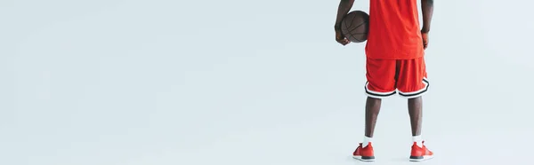 Vista cortada do jogador de basquete americano africano segurando bola no fundo cinza, tiro panorâmico — Fotografia de Stock
