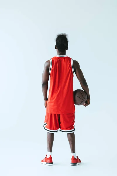 Vista posterior del jugador de baloncesto afroamericano sosteniendo la pelota sobre fondo gris - foto de stock