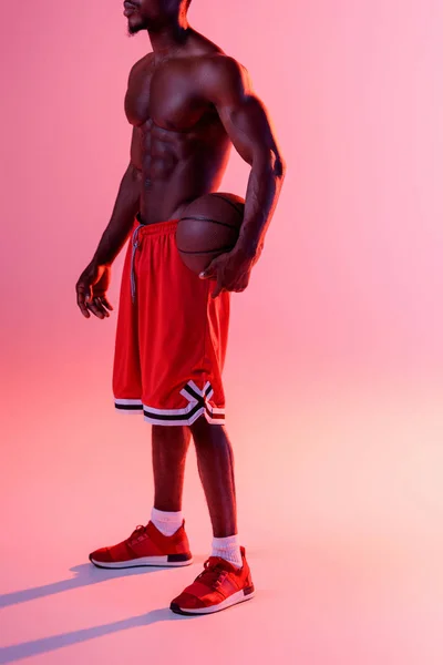 Partial view of african american sportsman holding ball on pink background with lighting and gradient — Stock Photo