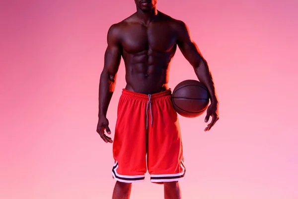 Обрезанный вид африканского американского спортсмена с мускулистым туловищем, держащего мяч на розовом фоне с градиентом — стоковое фото