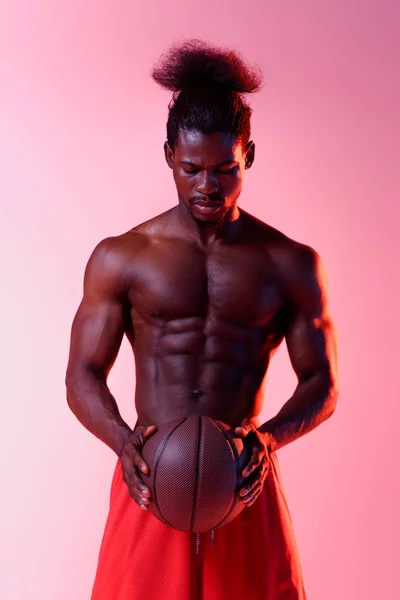 Shirtless, muscular african american basketball player holding ball on pink background with gradient — Stock Photo